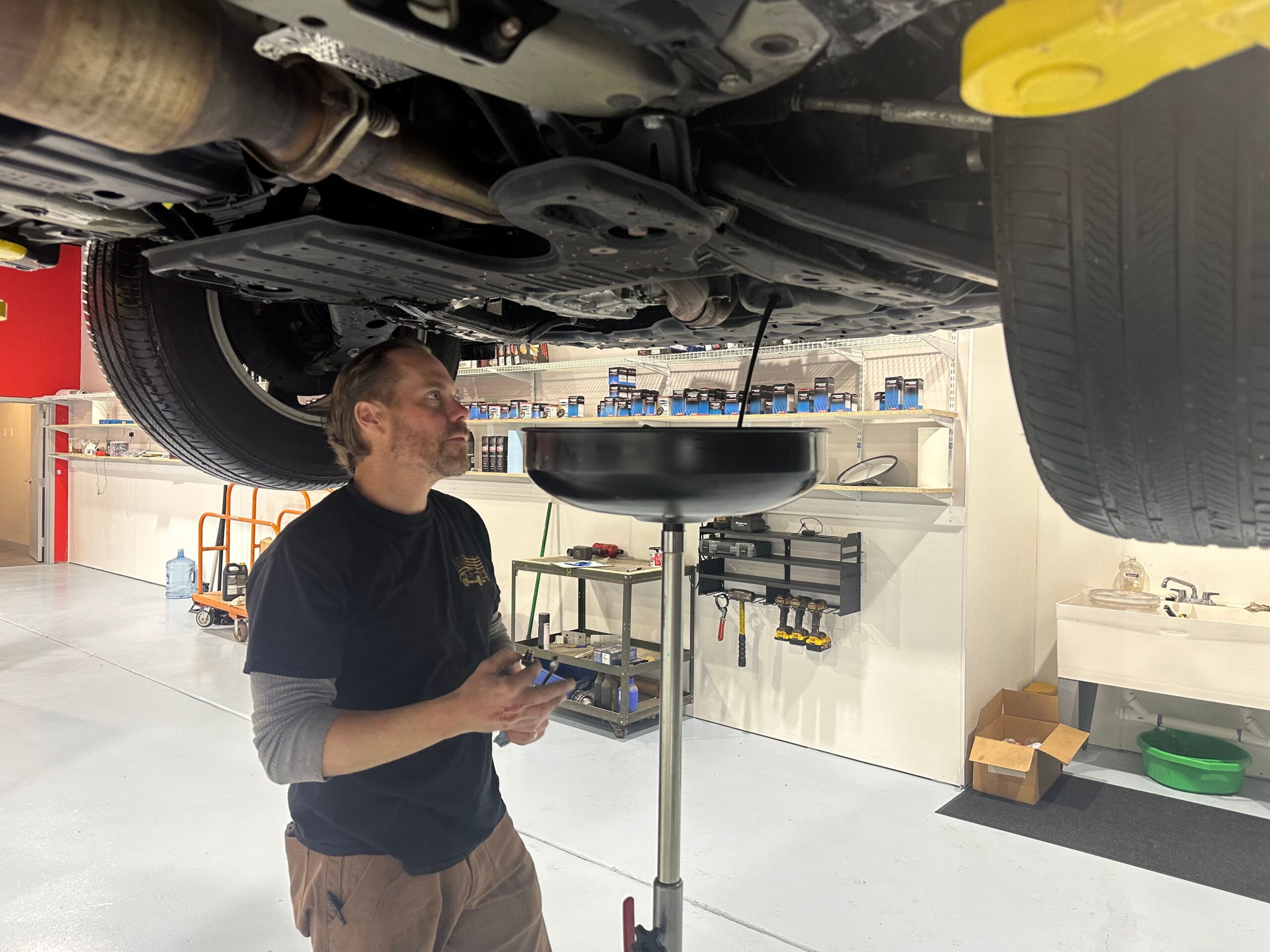 mechanic Jason Glemser conducting oil change observing oil drain as it drains out from vehicle